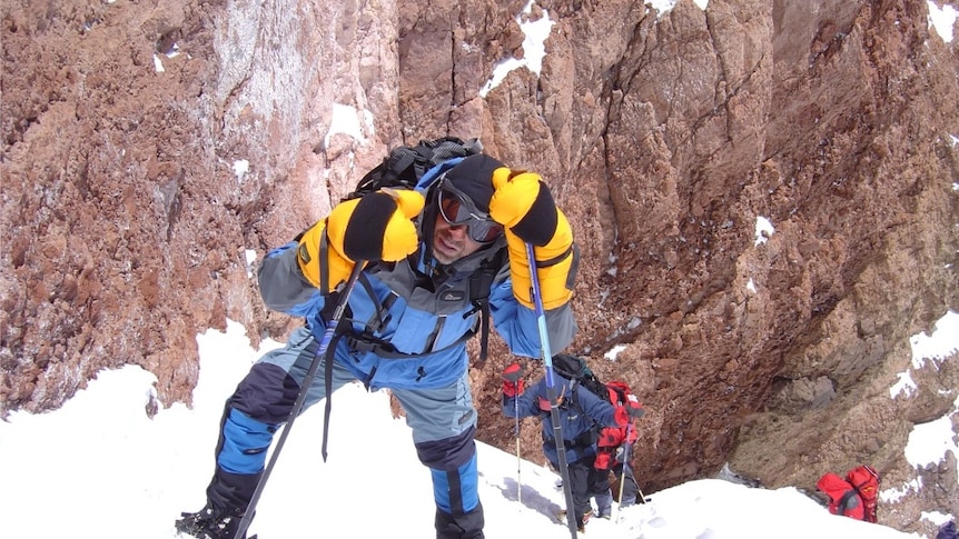 Dr Homayoun Jalali climbing a snowy mountain in a thick yellow and blue snow suit.