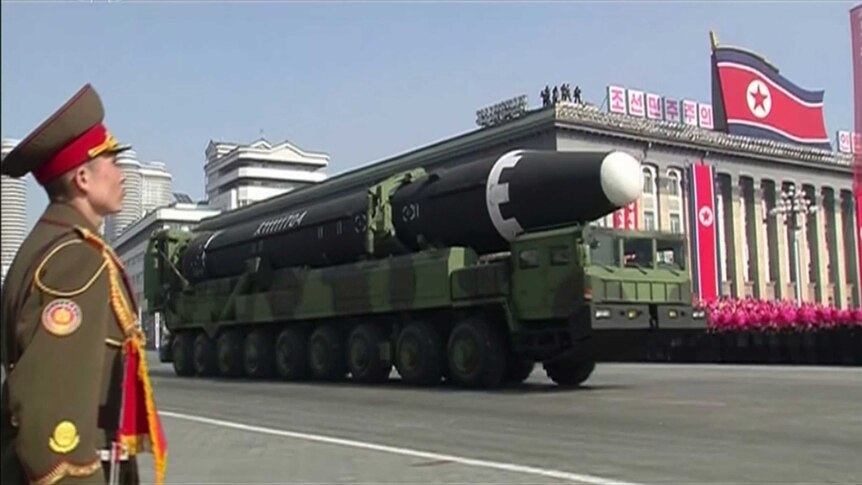 A soldier stands as a truck carrying a missile drives down a Pyongyang street.