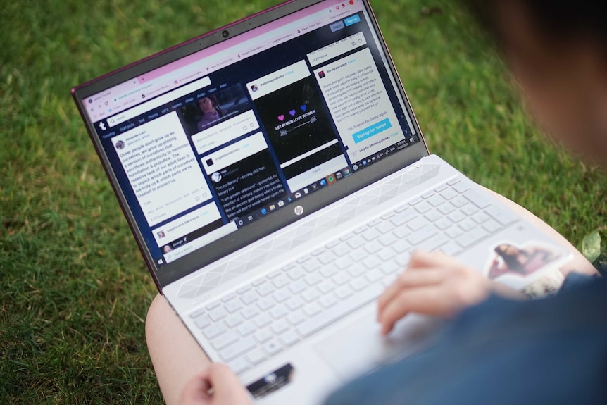 Kirra Hampson's hands are seen using the mouse pad of a computer while sitting on grass. Tumblr is on screen.