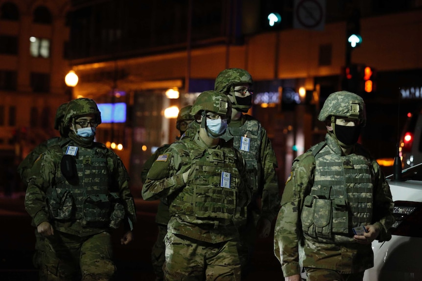A group of armed National Guard soldiers patrol a street at night