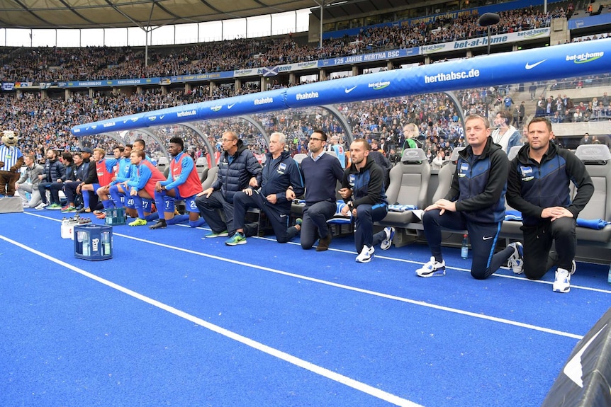 Hertha Berlin players and coaching staff take the knee during the German national anthem at a game in Berlin.