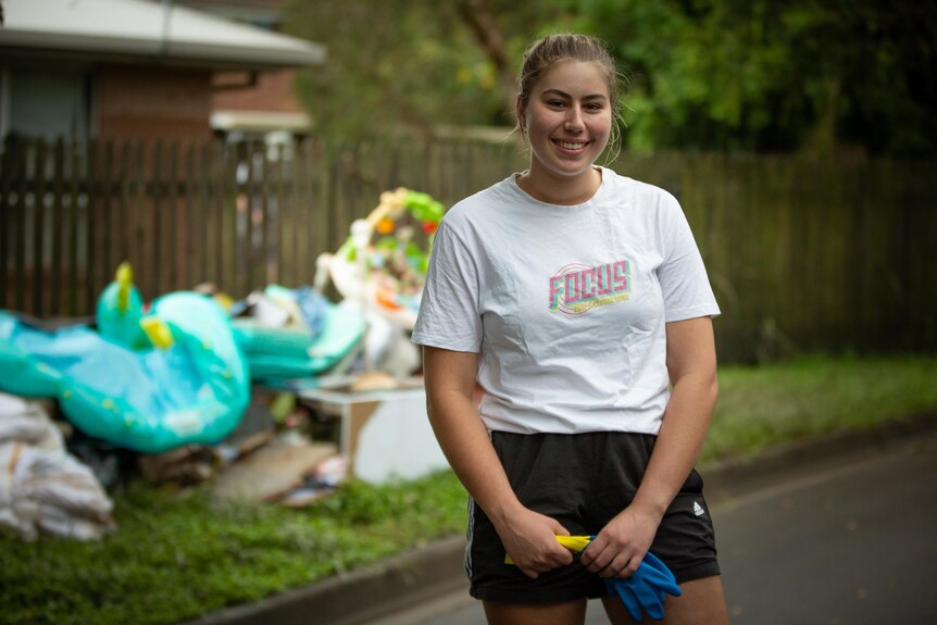 a woman in a white shirt smiles as she looks toward the camera in front of a pile of rubbish outside a home in Fairfield