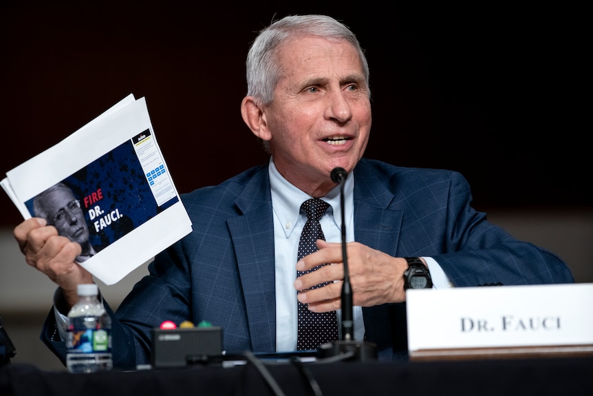 A man with silver hair and a blue suit speaks into a microphone.