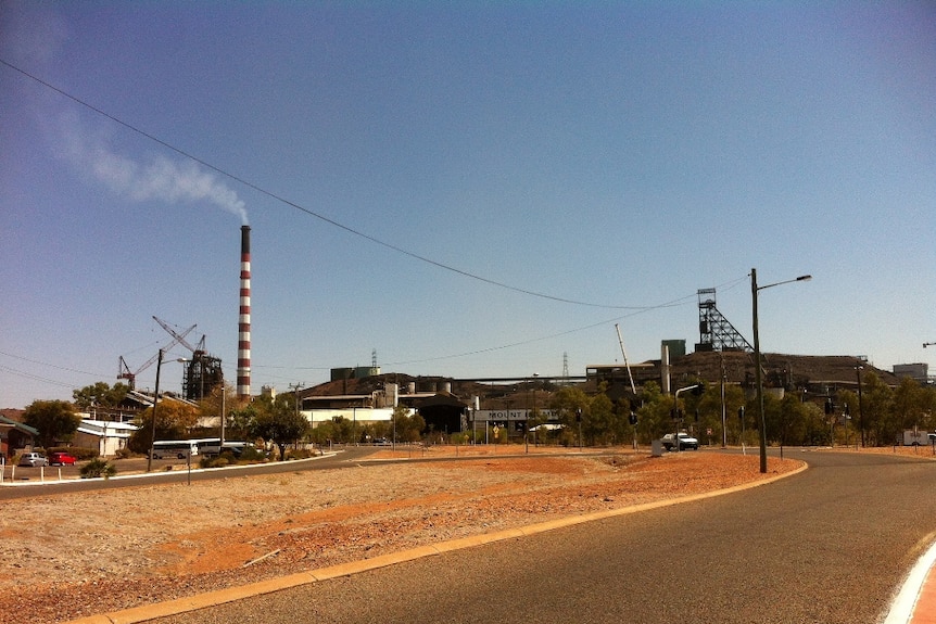 A red and white chimney towers over the Mount Isa mine. The landscape is brown and orange.