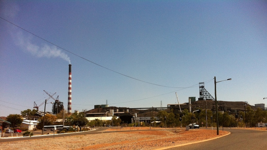 A red and white chimney towers over the Mount Isa mine. The landscape is brown and orange.