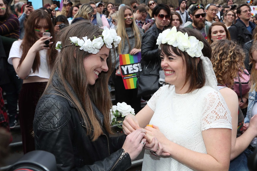 A woman puts a ring on the finger of another woman at a rally.