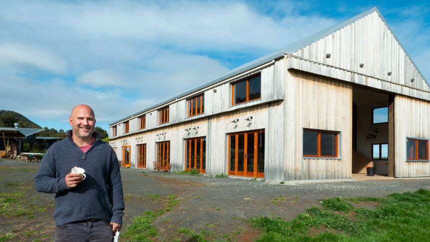 A man standing in front of large, new, barn-style building with many large windows