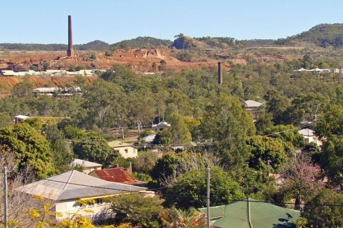 A view of the mining town of Mount Morgan, showing tin roofs of houses and an old mine and stack in the background.