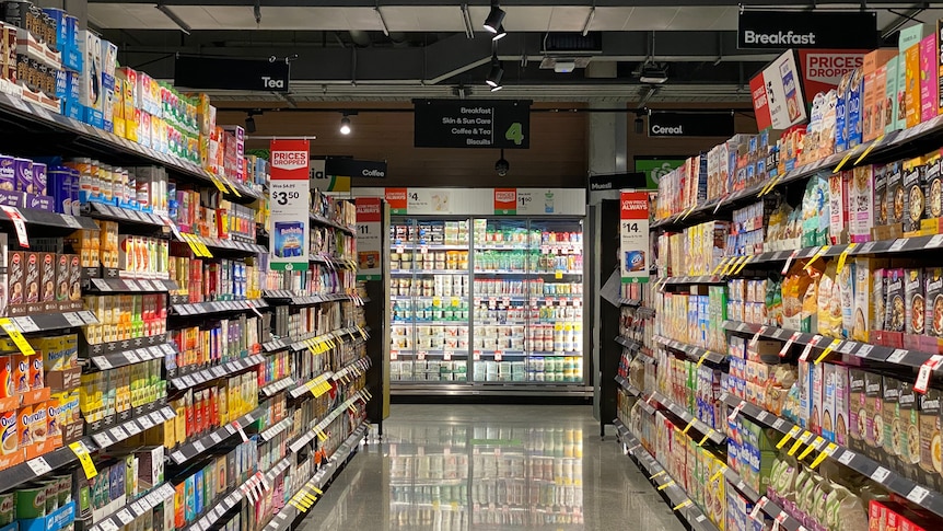 Interior of a supermarket, looking down an empty aisle lined with products.