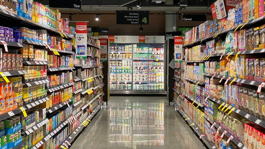 A supermarket aisle with grocery staples stacked on shelves on either side.