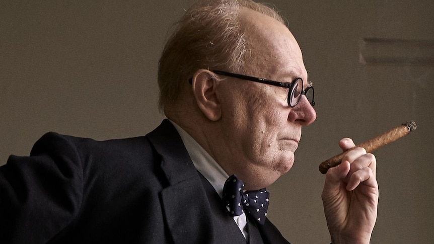 Actor Gary Oldman with prosthetic make-up as Winston Churchill, wearing a bow-tie and holding a cigar.