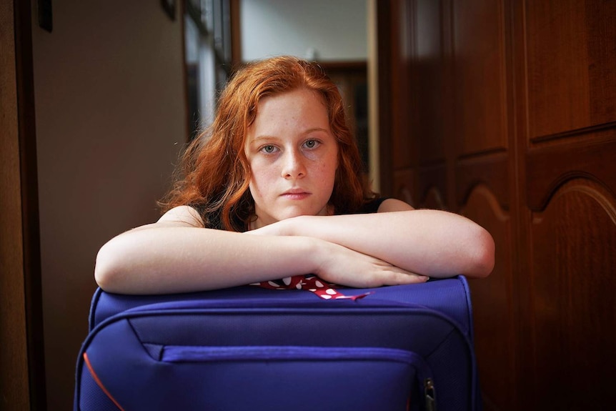 Headshot of teenager Adelaide Hardy leaning on a suitcase in her house.