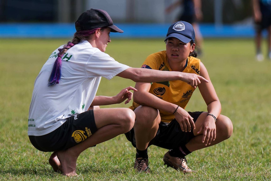 Woman crouches down on the field next to a player to give her ultimate frisbee coaching advice