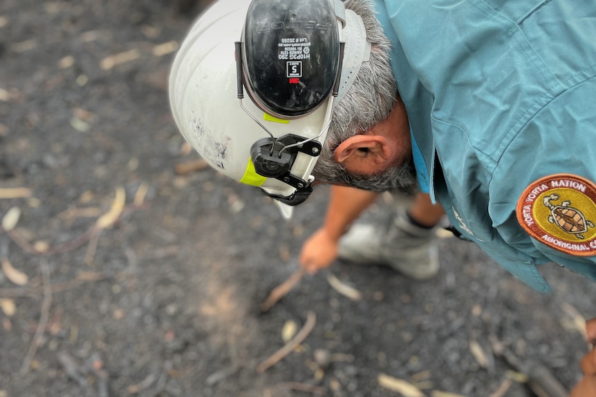 A man scrapes a stick through ash on the ground