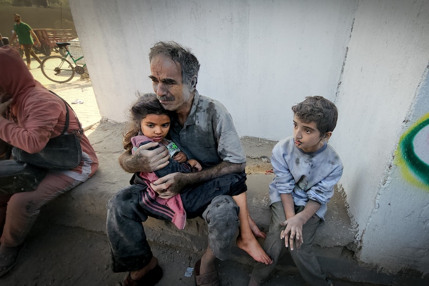 An older man covered in dust clutches a little girl on his lap 