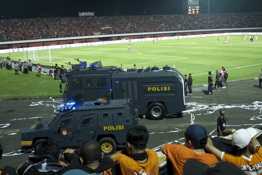 Two armoured police vehicles at next to a football pitch.