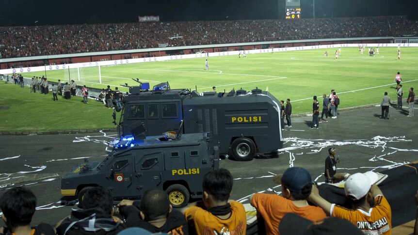Two armoured police vehicles at next to a football pitch.