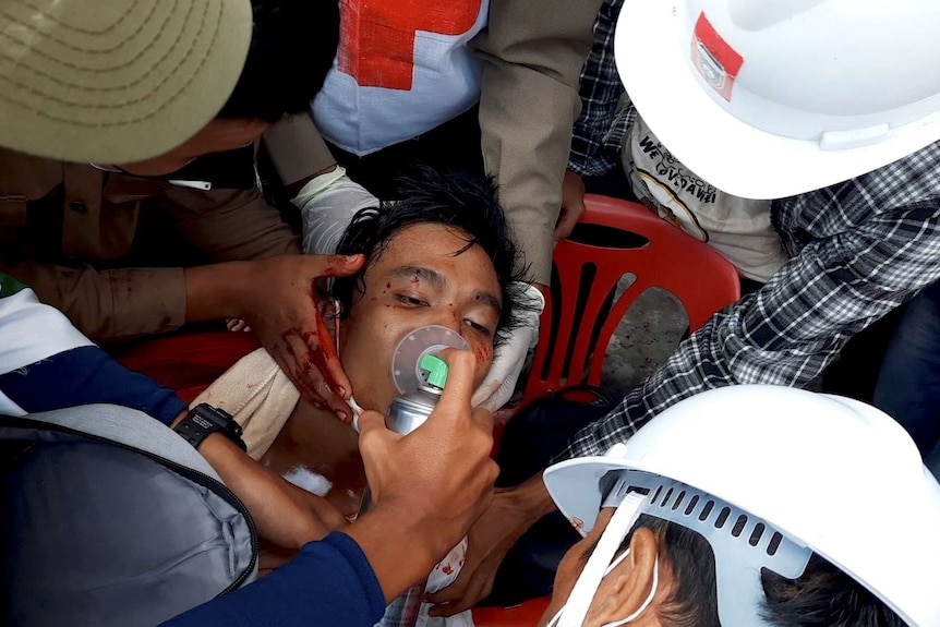 An injured young man lying on the ground is given oxygen as he's surrounded by medical staff.