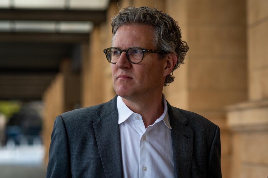 A man with a suit and glasses, with grey curly hair