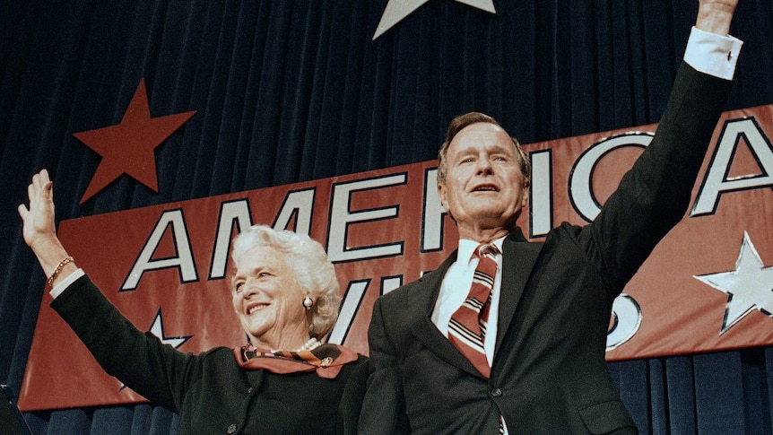 a man and a woman stand with an arm raised in front of a sign saying America