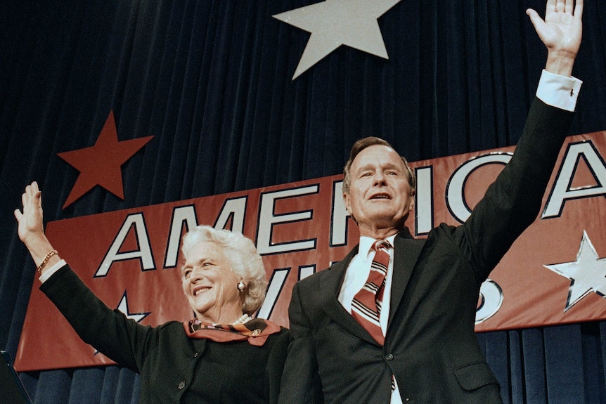 a man and a woman stand with an arm raised in front of a sign saying America