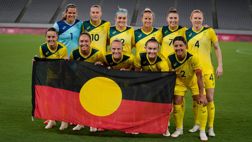 Australia's women's football team, the Matildas, pose with the Aboriginal flag before their first game of the Tokyo Olympics.