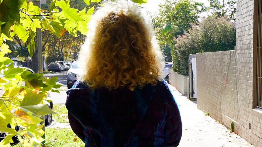 The back of a woman with curly blond hair standing on the street.