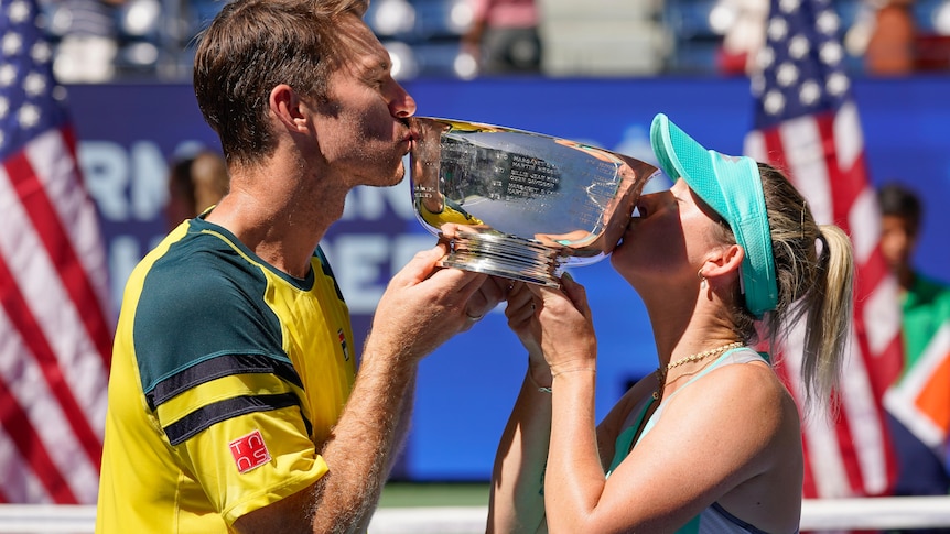 John Peers and Storm Sanders kiss either side of the US Open mixed doubles trophy