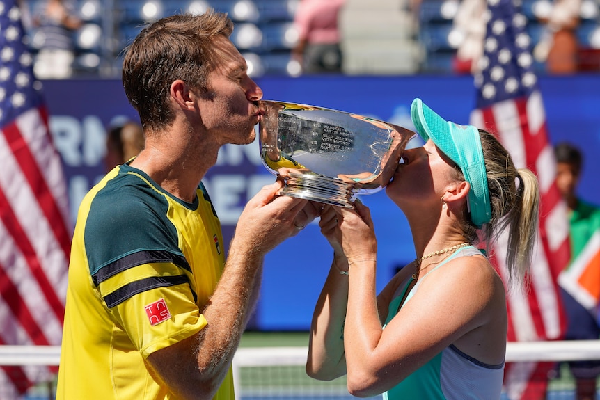 John Peers and Storm Sanders kiss either side of the US Open mixed doubles trophy