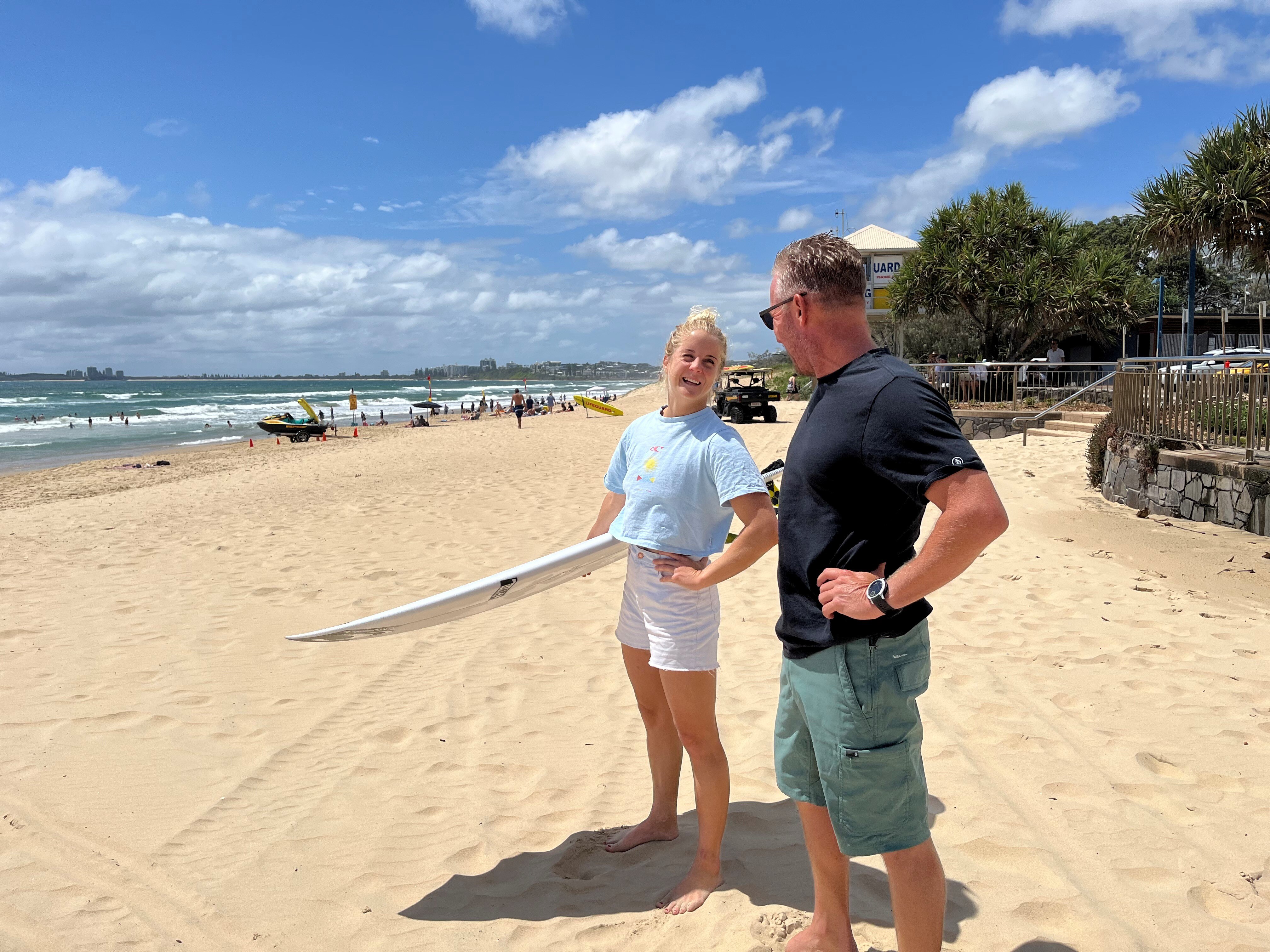 Woman on beach holding surfboard and laughing with man