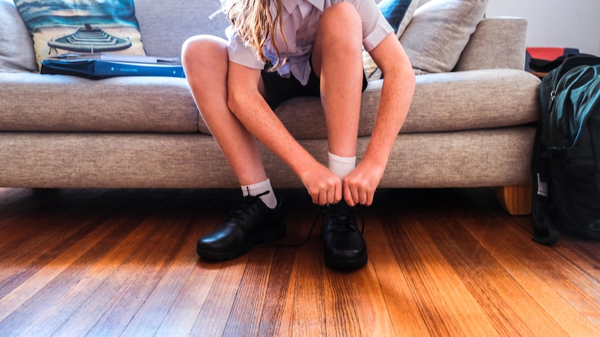 A child in school uniform puts shoes on.