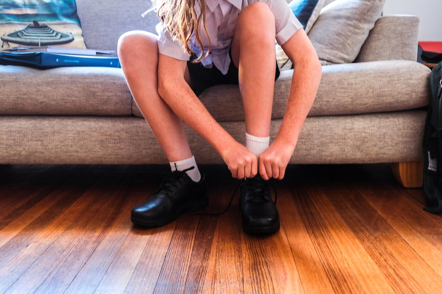 A child in school uniform puts shoes on.