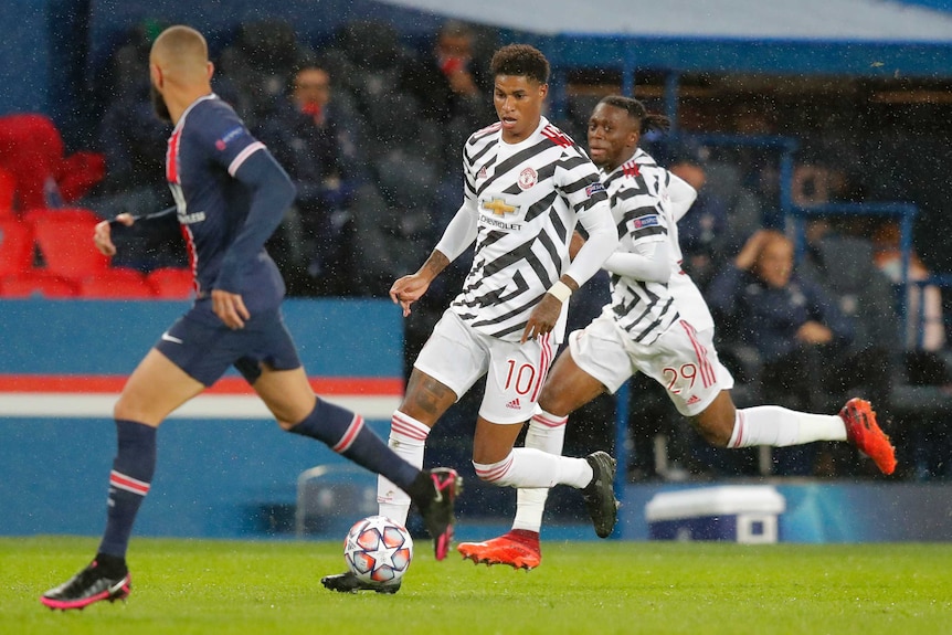 Marcus Rashford runs with a football at his feet, wearing a white and black zebra-style football shirt