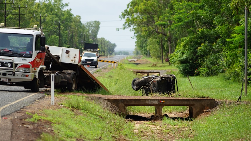 Emergency vehicles are by the edge of the road where a ATV is on its side.