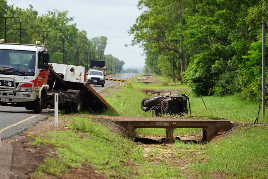 Emergency vehicles are by the edge of the road where an ATV is on its side.