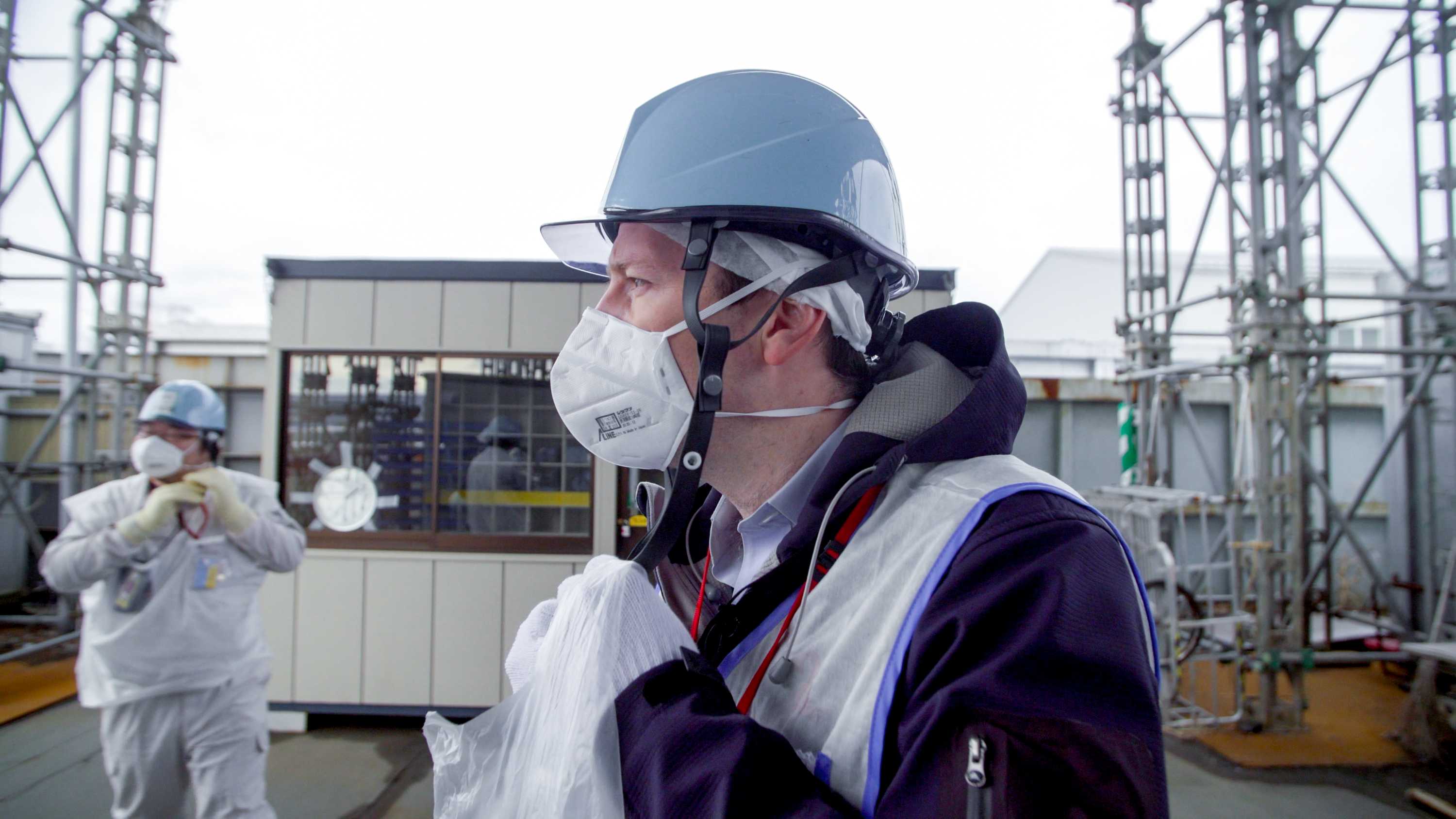 一名戴着头盔、面罩和背心的男子站在核电站外