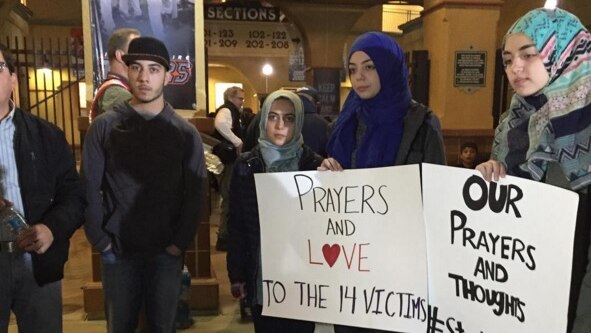 A young Muslim woman holds a sign reading "Prayers and love to the 14 victims".