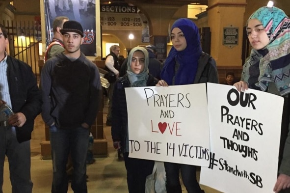 A young Muslim woman holds a sign reading "Prayers and love to the 14 victims".