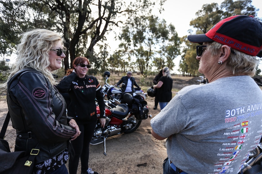 A group of women in motorcycle gear stand around their bikes having what appears to be a friendly conversation.