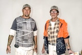 Two men in paint stained clothes and matching baseball caps hold buckets of paint.