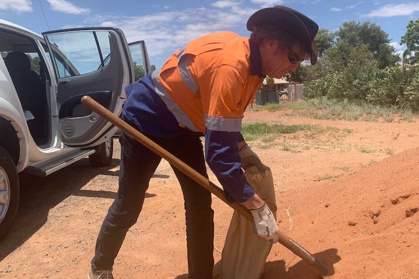 A man in an orange high-viz top shovels sand into a sandbag.