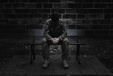 An unidentifiable male sits on a bench wearing an Army uniform
