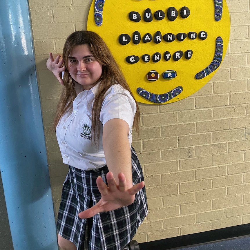 Penelope poses with her hands outstretched in front of a sign that says "Muru Bulbi Learning Centre".