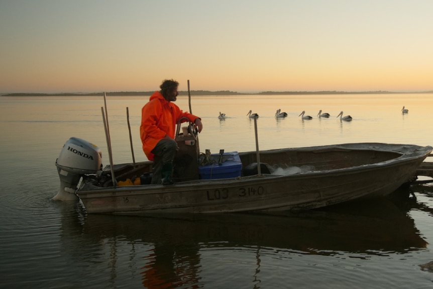 Glen Hill on a fishing boat in the Coorong with pelicans swimming in the background.