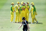 Australian players hug in a large group as a New Zealand player wearing black walks in the foreground