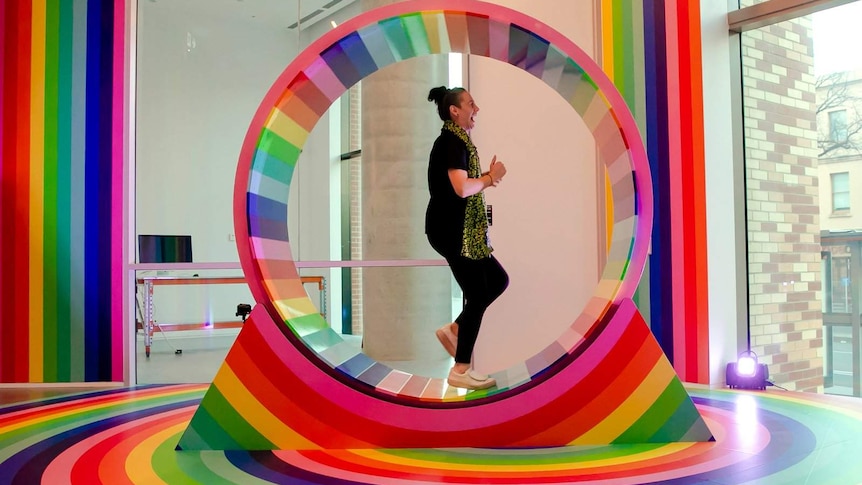 Woman running and laughing inside a multi-coloured hamster wheel.