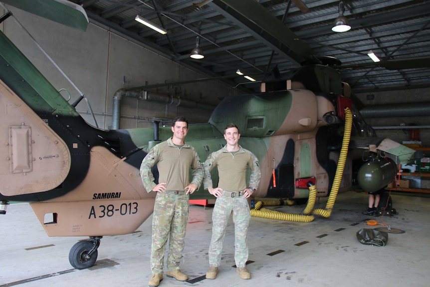 Two young men in army camouflage standing before a Tiger helicopter, their hands on their hips