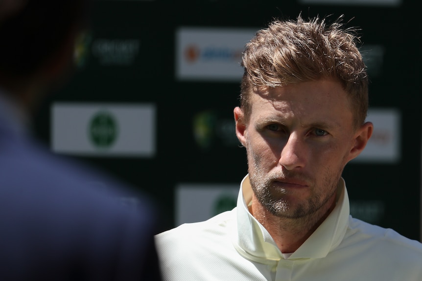 England cricket captain Joe Root watches an interviewer whose shoulder is blurred in the foreground.