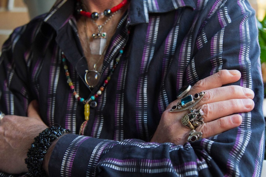 Close up of Marque Caban's chest and hands, showing stone jewellery.