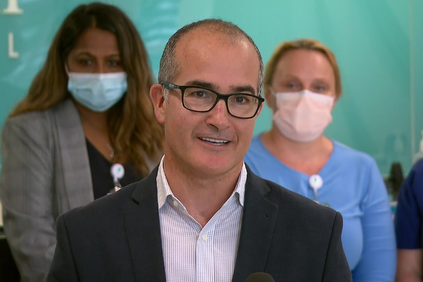 James Merlino standing in front of three masked women